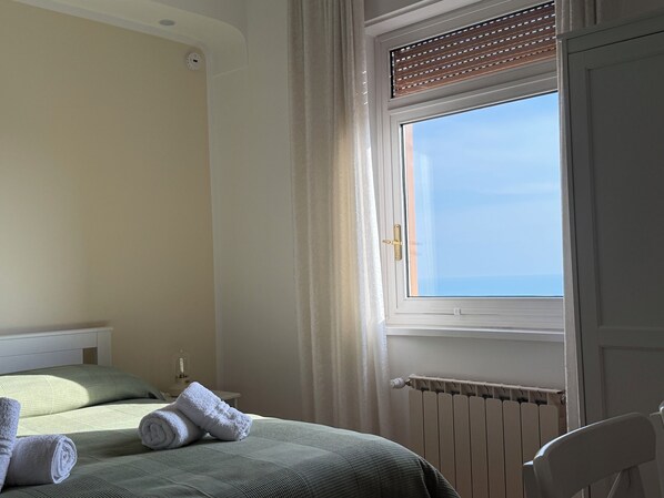 A bedroom with two beds, a window with blinds, a radiator, and a chair.