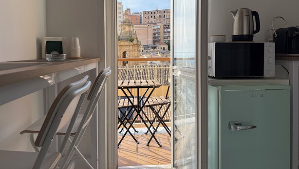 Un balcon avec vue sur les immeubles, une petite cuisine équipée d’un four à micro-ondes, d’une bouilloire et d’un grille-pain, ainsi qu’une chaise.