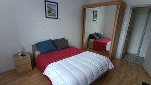 Un dormitorio con cama, mesita de noche, espejo y un cuadro en la pared.