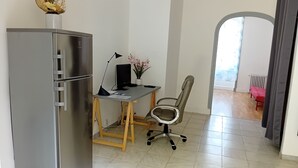 Un espacio habitable compacto con kitchenette, un escritorio con computadora, una silla y vistas a un balcón a través de un arco.