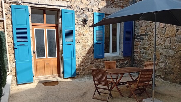Un edificio de piedra con contraventanas azules, una puerta de madera y una mesa con sillas.