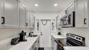 Una cocina compacta con armarios blancos, microondas, estufa y cafetera.