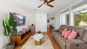 A modern living room with a ceiling fan, a large flat-screen TV, a wooden entertainment unit, a coffee table, and a sofa with patterned cushions. - Family house,3 Rooms,4Beds, 5 to 8 People,Pet-Friendly Big Yard lots of Parking (Duffy)