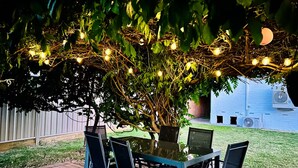 An outdoor patio with a table and chairs, surrounded by greenery and string lights. - Family house,3 Rooms,4Beds, 5 to 8 People,Pet-Friendly Big Yard lots of Parking (Duffy)