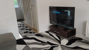 Ein Zimmer mit Fernseher auf Holzfuß, einem Teppich mit ZEBRA-Muster, einem weißen Heizkörper und einer Tür zu einem weiteren Raum.