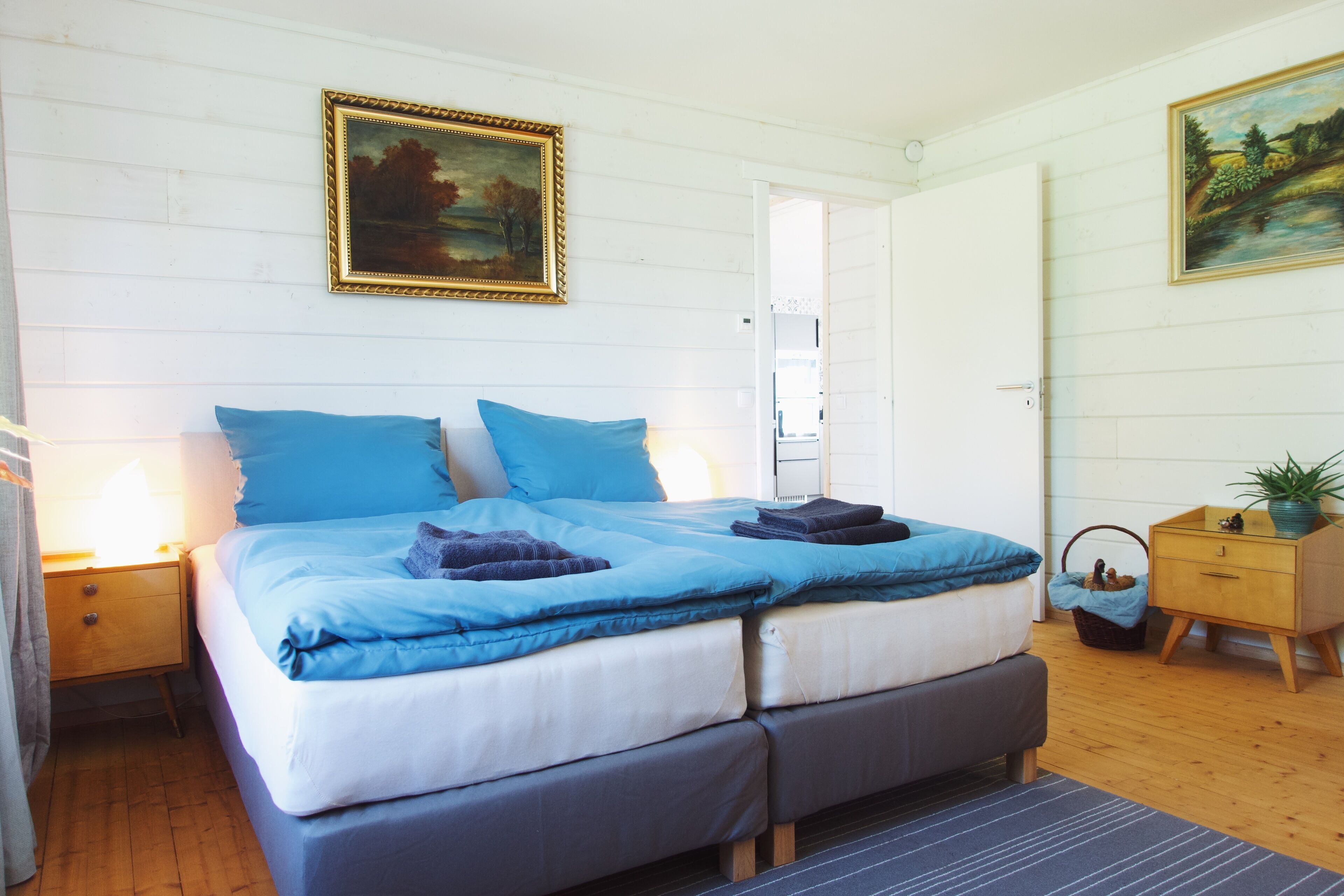 Een slaapkamer met een tweepersoonsbed, twee nachtkastjes, een houten dressoir en een schilderij aan de muur.