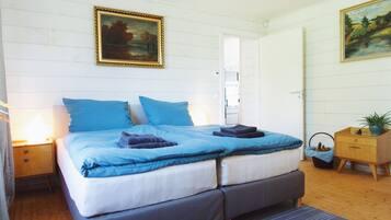 Een slaapkamer met een tweepersoonsbed, twee nachtkastjes, een houten dressoir en een schilderij aan de muur.