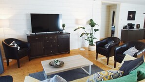 A living room with a flat-screen TV, dark wooden cabinet, two leather chairs, a green sofa, and a coffee table.