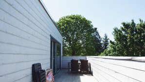 A wooden deck with a table and chairs, a flag, and a building with white siding.