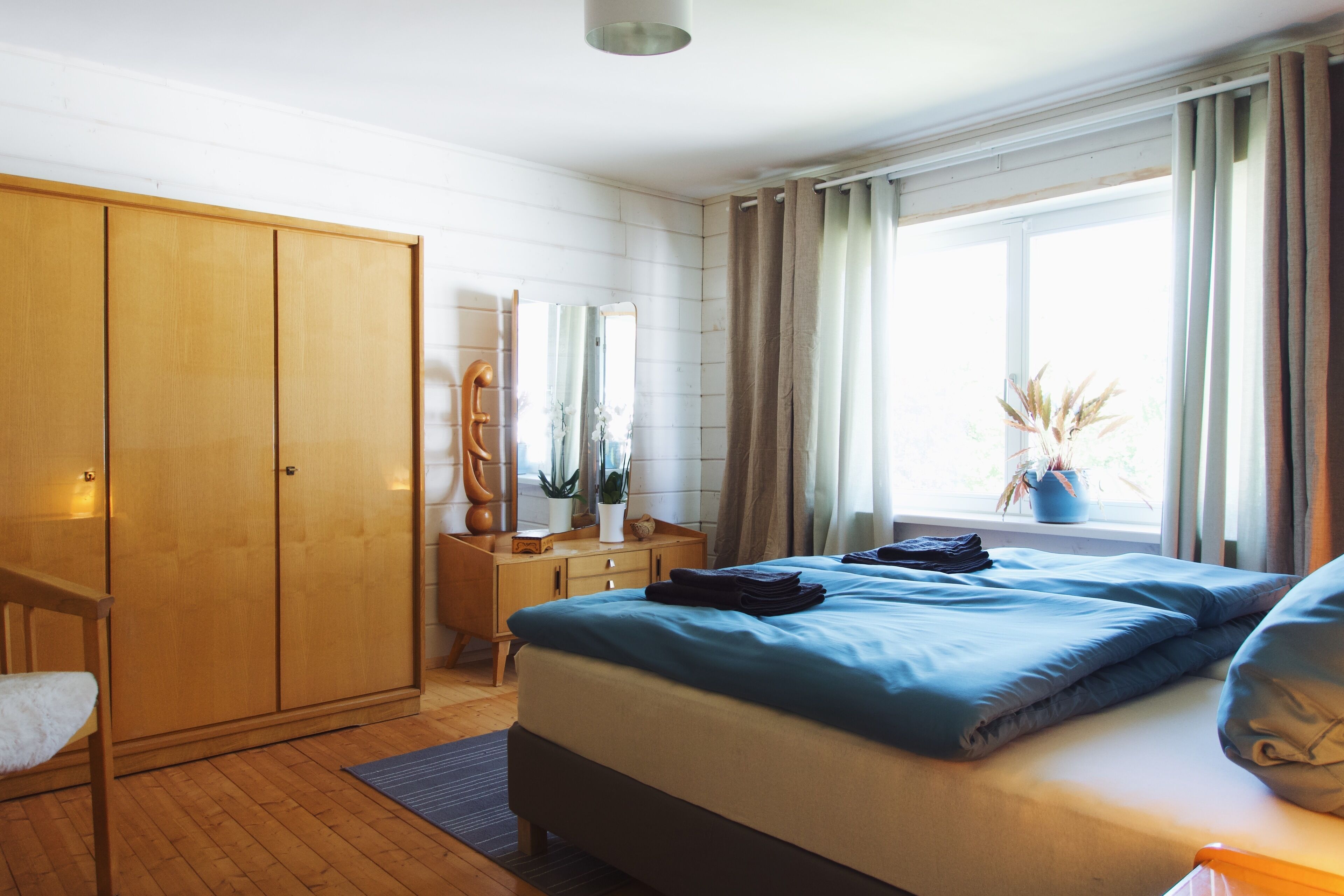 Ein Schlafzimmer mit Bett, Holzschrank, Nachttisch und einem fenster mit Vorhängen.