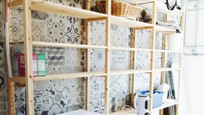 A laundry room with a front-loading washing machine, wooden shelving with patterned tiles, and a basket on the top shelf.