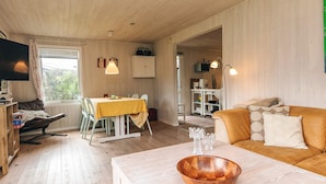 Una sala de estar acogedora con suelo de madera, un comedor con mesa y sillas, un sofá con cojines y un televisor sobre un mueble.