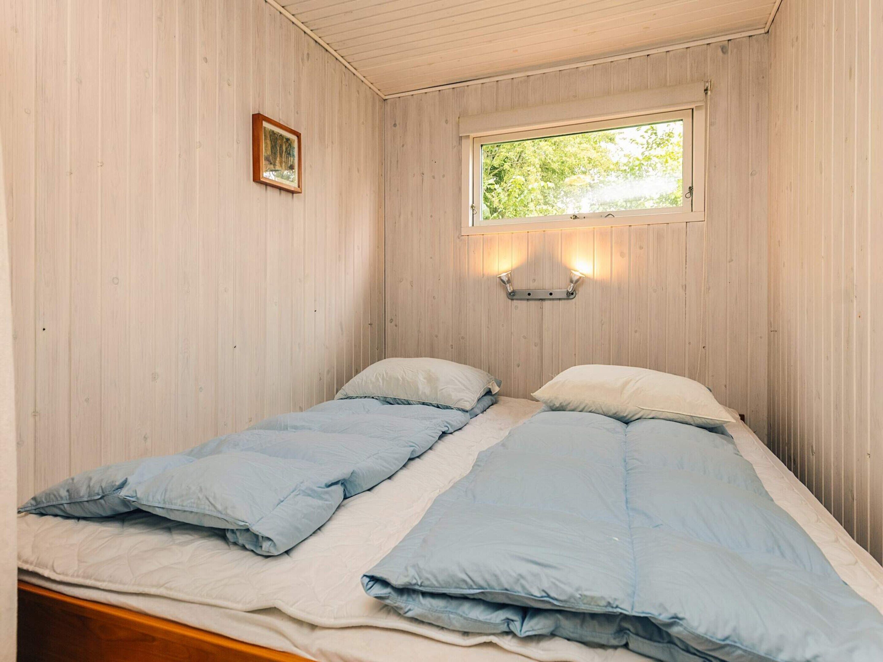 Pieni, yhden huoneen kokoinen majoituspaikka, jossa on kaksi sänkyä, ikkuna, josta avautuu näkymä vehreään maisemaan, ja seinälle asennettu valaisin.