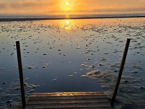 Une jetée en bois s’étendant sur une étendue d’eau calme, avec un coucher de soleil en arrière-plan.