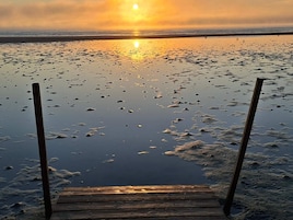 A wooden pier extending into a calm body of water with a sunset in the background.