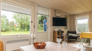 Una sala de estar acogedora con una mesa de madera, un televisor y vistas al verdor exterior.