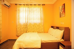 Cozy retreat with a single bed, nightstand, and painting above, set against a warm backdrop.