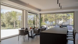 Una cocina moderna con una isla grande, comedor con sillas y ventanas amplias que ofrecen vistas a la vegetación.