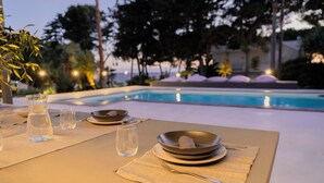 Mesa para dos personas con vista a una piscina y árboles al fondo.