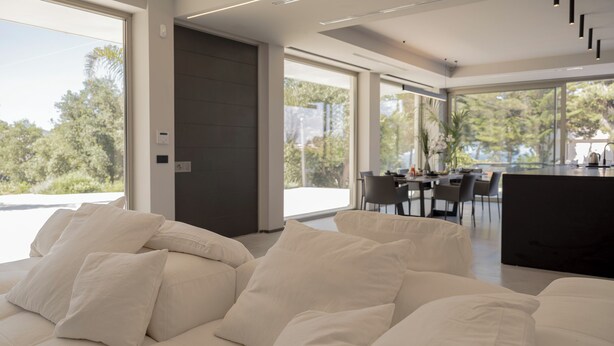 Una sala de estar moderna con un sofá beige grande, una puerta oscura y un comedor con sillas y una mesa.