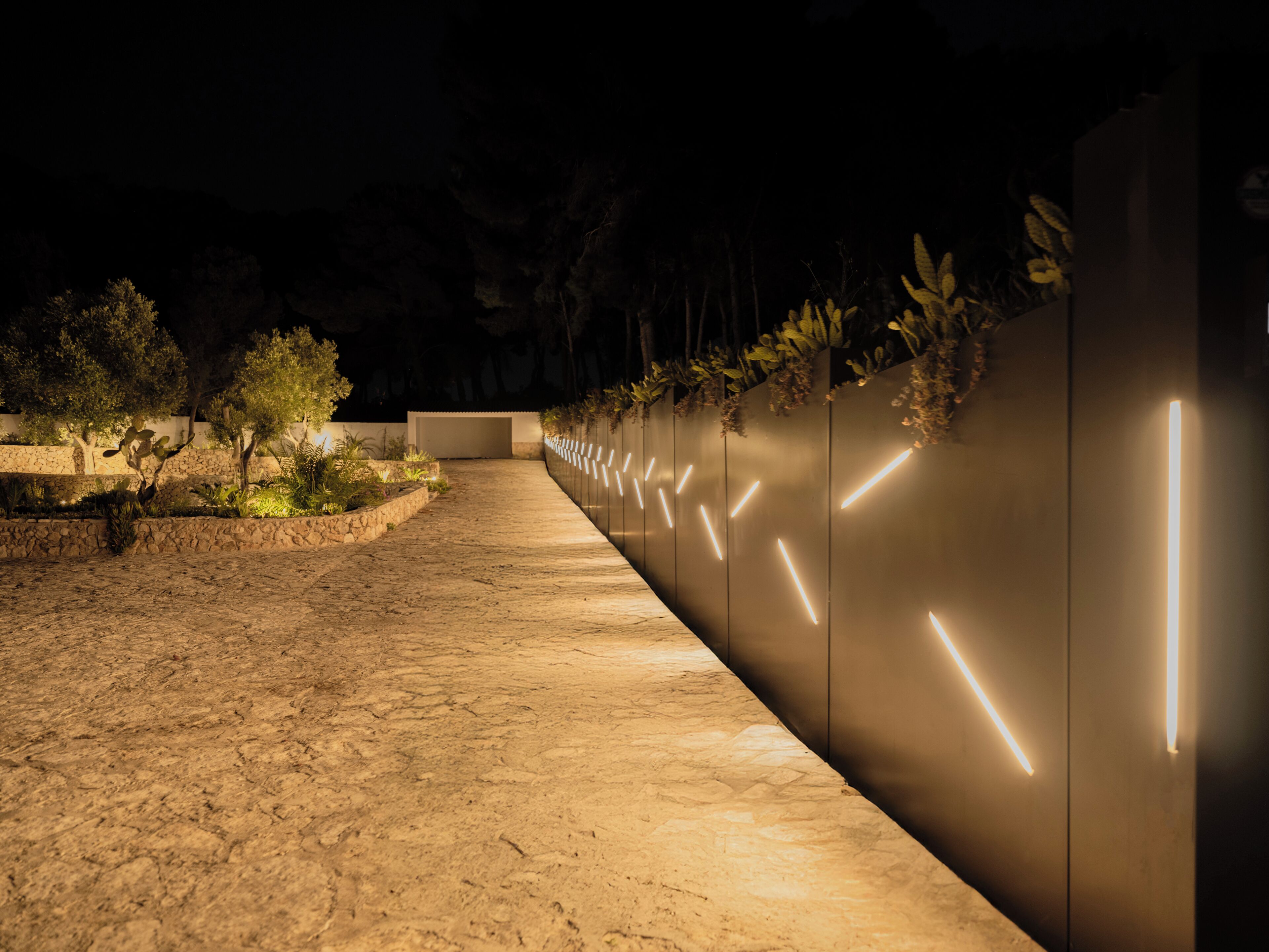 Un sendero nocturno con líneas iluminadas en una pared, que lleva a un edificio.