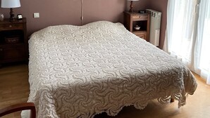 A bedroom with a large bed, a chandelier, a bedside table with a lamp, a dresser, and a window with curtains. - Quiet and surrounded by nature 10 mm from the A75 freeway (Montcel)