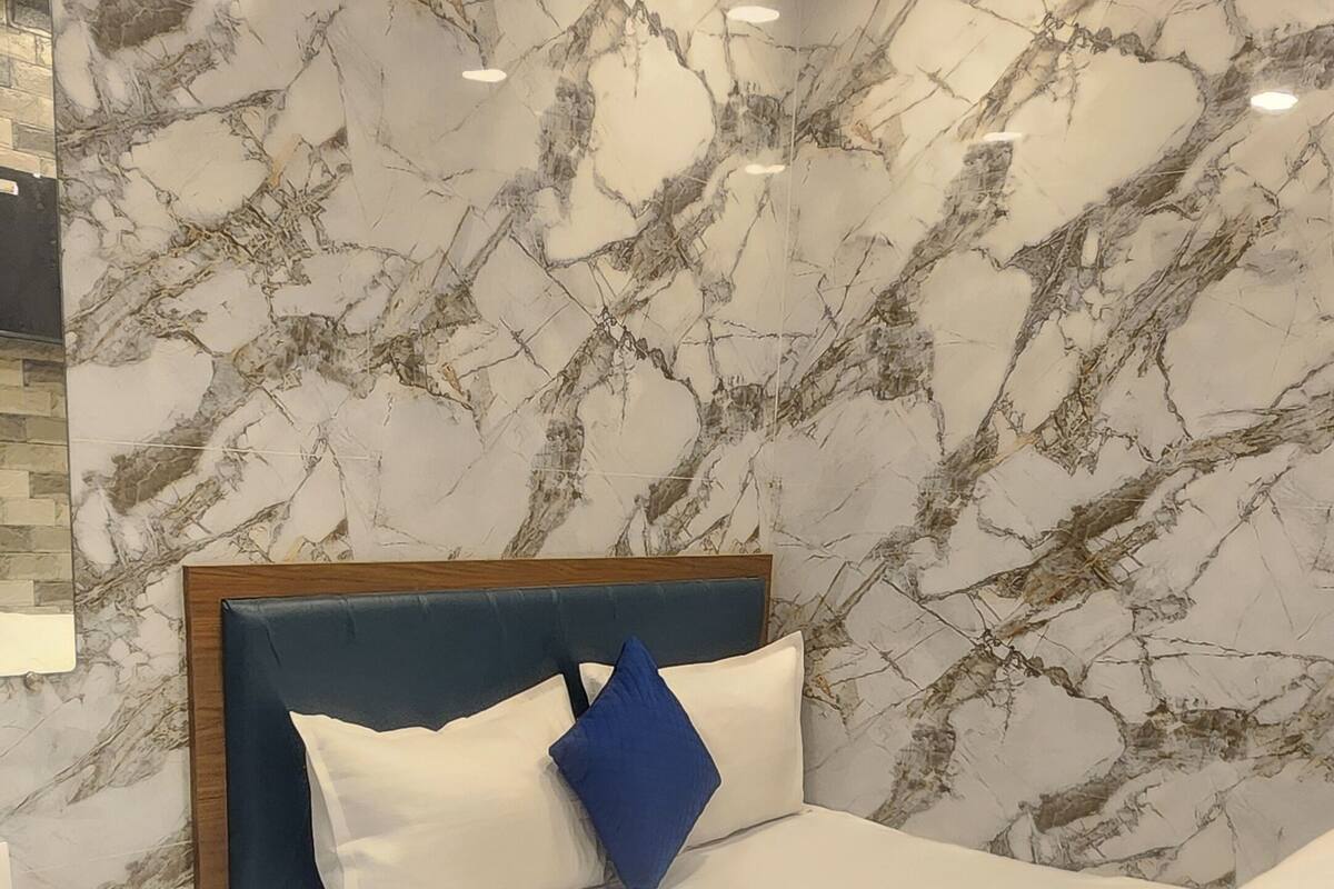 A bedroom with a bed, wooden nightstand, marble-patterned walls, and ceiling lights.