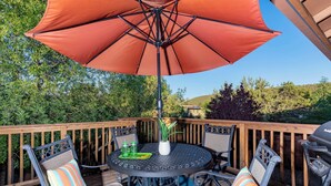 Une table ronde entourée de chaises, un parasol et un barbecue sur une terrasse en bois.