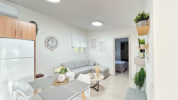 A modern kitchen with white cabinets, a Bosch refrigerator, a dining table with chairs, a gray sofa, and a small round table with a vase. - QUIET ESCAPE (CHORA MESSINIAS)
