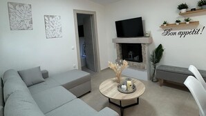 A modern living room with a grey sectional sofa, a round coffee table with decorative items, a flat-screen TV mounted above a fireplace, and a small bench. - QUIET ESCAPE (CHORA MESSINIAS)