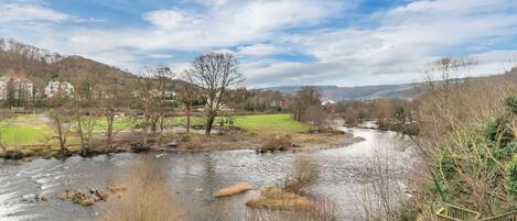 A river flowing through a rural landscape with houses and a grassy field in the background.