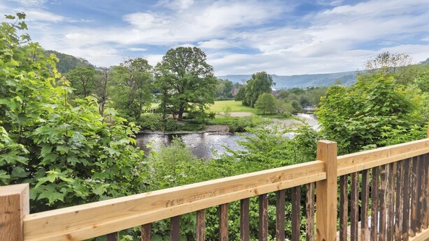 Una terraza de madera con vistas a un río, árboles y un campo de golf al fondo.