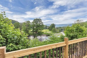 Una terraza de madera con vistas a un río, árboles y un campo de golf al fondo.