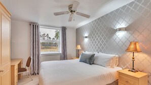 Un dormitorio con cama, escritorio, silla, ventilador de techo y ventana con cortinas.