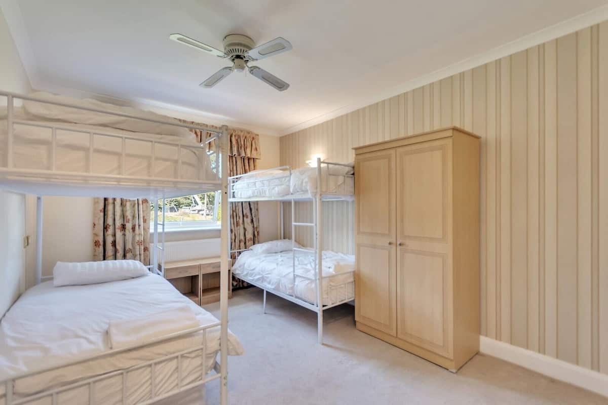 A bunk bed room with a ceiling fan, a wooden wardrobe, and a window with curtains.