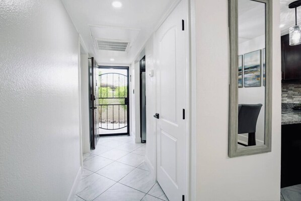 A hallway with white walls, a tiled floor, and a door with a black metal gate leading outside.
