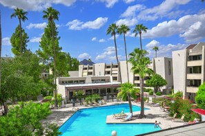 A swimming pool surrounded by palm trees and a building with balconies.