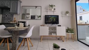 A modern kitchen with a dining area, a TV on a white cabinet, and a balcony with a view.