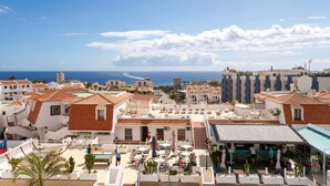 A coastal residential area with terracotta-tiled roofs, outdoor seating, and a pool.