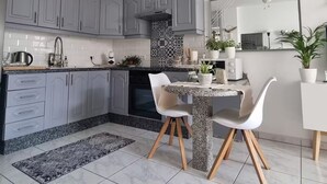 A modern kitchen with grey cabinets, a granite countertop, and a dining area with a marble floor.