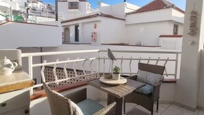 A balcony with wicker furniture, a table with a teapot, and a view of white buildings with red roofs.