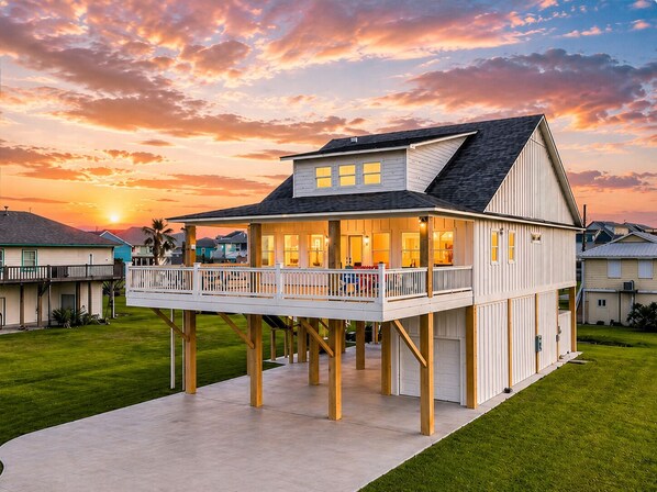 A two-story house with a balcony, a garage, and a well-maintained lawn. - Sea the Light | Sleeps 14 | Tiki Bar + Fire Pit + Putt-Putt (Crystal Beach)