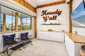 Una habitación con un ventanal grande, techo de madera, mostrador de recepción y dos sillas plegables.