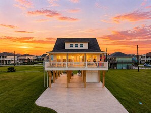 A waterfront house with a deck, a garage, and a grassy lawn.