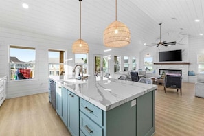 A spacious kitchen with a large island, pendant lights, and a ceiling fan. - Sea the Light | Sleeps 14 | Tiki Bar + Fire Pit + Putt-Putt (Crystal Beach)