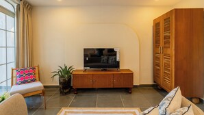 A living room with a television on a wooden cabinet, a sofa, and a large wooden wardrobe. - Hotel Green Park (New Delhi)