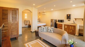 A modern kitchen with a refrigerator, microwave, and sink. There is a sofa with floral cushions in the living area. - Hotel Green Park (New Delhi)
