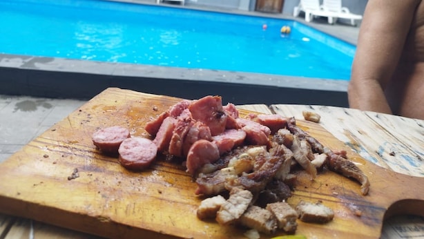A wooden cutting board with sliced meats in front of a swimming pool. - Corporate Accommodation (Parque das Universidades Campinas)