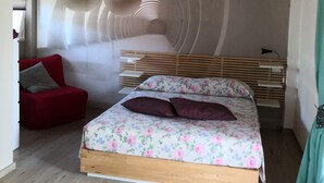 A bedroom with a wooden ceiling, a bed with floral bedding, a red chair, and a wall mural. - A peaceful stay through culture and relaxation. Directly on the lake (Villaggio Sanghen)