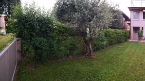 A two-story house with a curved roof, a front porch with outdoor seating, and a well-maintained lawn. - A peaceful stay through culture and relaxation. Directly on the lake (Villaggio Sanghen)